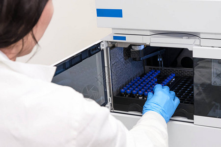 穿着白色实验室外套的科学家将装有样品的小瓶放入HPLC系统的自动进样器中化学实验室的高效液相色谱药物图片