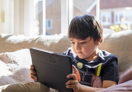 高调的孩子坐在沙发上看平板电脑上的卡通片背景图片