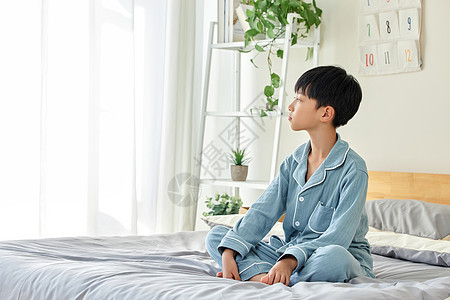 早晨穿睡衣坐在床上的小男孩图片