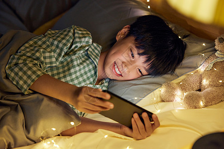 小男孩在床上玩手机图片