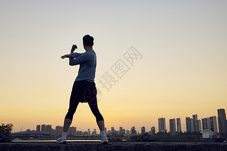年轻运动男性夕阳下运动拉伸剪影图片