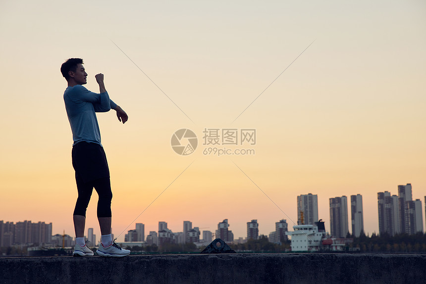 夕阳下男青年运动拉伸背影图片