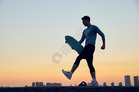 城市傍晚男青年拿着滑板行走图片