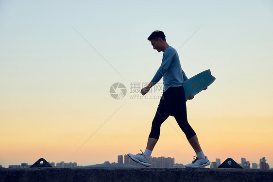 男青年傍晚拿着滑板行走图片