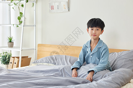 穿睡衣坐在床上的小男孩高清图片