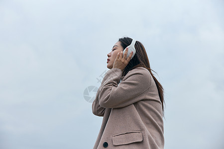 年轻女性在江边带着耳机伤感情绪背景图片