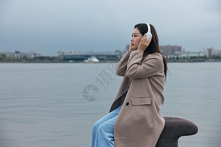 年轻女性在江边带着耳机伤感情绪背景图片