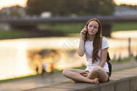 日落时坐在滨海边的可爱女孩在手机上讲图片