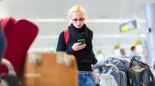休闲的金发年轻女子在排队办理登机手续和行李托运时使用手机使人们能够访问互联网连接的无线网络热图片