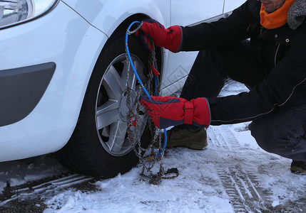 在冬季雪上在汽车轮胎中安装雪链的图片