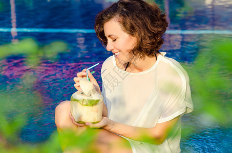 在游泳池附近喝椰子鸡尾酒的女人图片