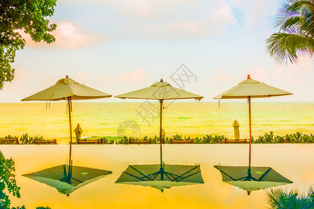 漂亮的豪华雨伞和椅子在酒店度假村的海滩和大海附近的游泳池周围图片