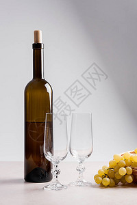 浅色大理石背景上的两个空酒杯和棕色瓶白葡萄酒一串绿色葡萄放在眼镜附近图片