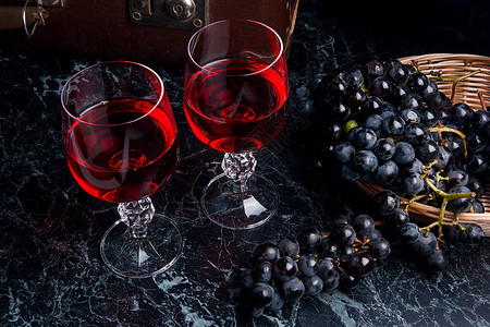 两杯红酒在深色大理石背景上深色大理石背景上的蓝色成熟葡萄黄色篮子里的成熟葡萄和背图片