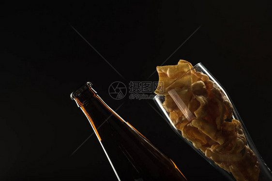瓶装和杯子里的金啤酒黑底带泡沫和零食坚果图片