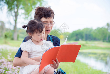 亚洲祖母为她在公园的孙女读书给在公园图片