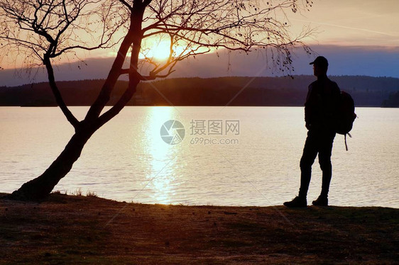 身着深色运动服背着运动背包的高个子徒步旅行者站在海滩上图片