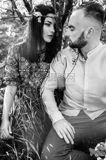 美丽的夫妇在盛开的花园里留着胡子的时尚男人和化着温和妆容的女孩坐在树下的草地图片