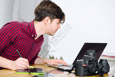 在办公室用笔记本电脑工作的可爱的年轻人使用图形平板图片