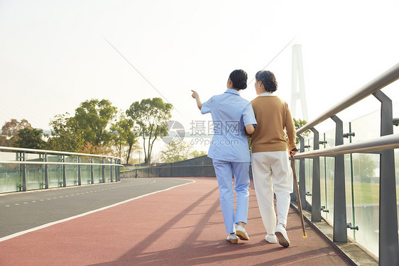 女护工陪伴老人公园散步背影图片