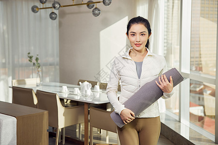 室内抱着瑜伽垫的女性图片