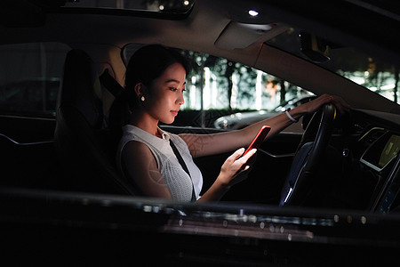 繁华夜景夜晚青年女人坐在汽车里使用手机背景