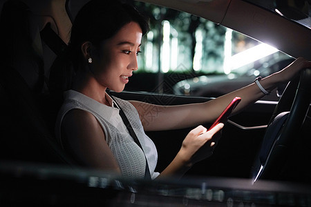 夜晚青年女人坐在汽车里使用手机图片