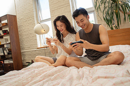 青年情侣趴在床上玩手机图片