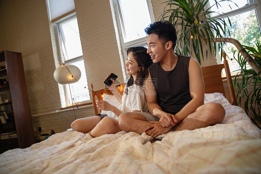 青年情侣坐在床上看手机图片