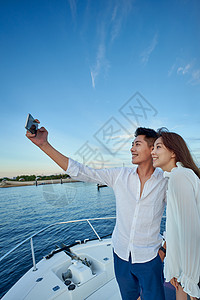 青年夫妇站在游艇上用手机拍照高清图片