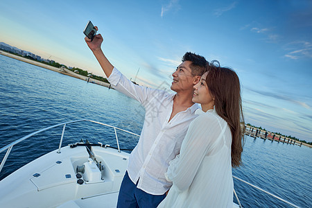 青年夫妇站在游艇上用手机拍照图片