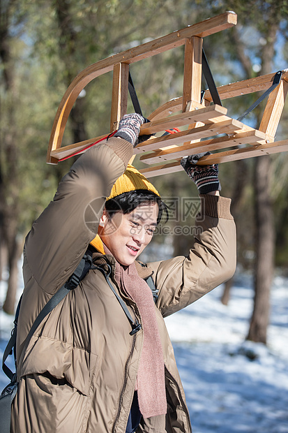 雪地上步行举着雪橇的青年男人图片