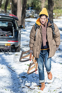 雪地上步行拿着雪橇的青年男人图片