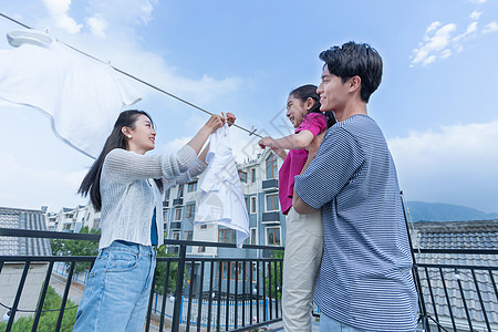 年轻爸爸抱着女儿和妈妈一起晾衣服图片