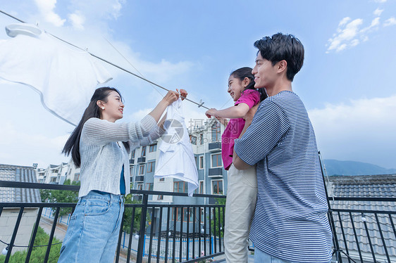 年轻爸爸抱着女儿和妈妈一起晾衣服图片