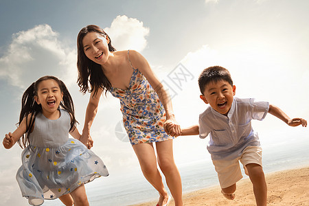 年轻母亲牵着两个孩子在沙滩上奔跑图片