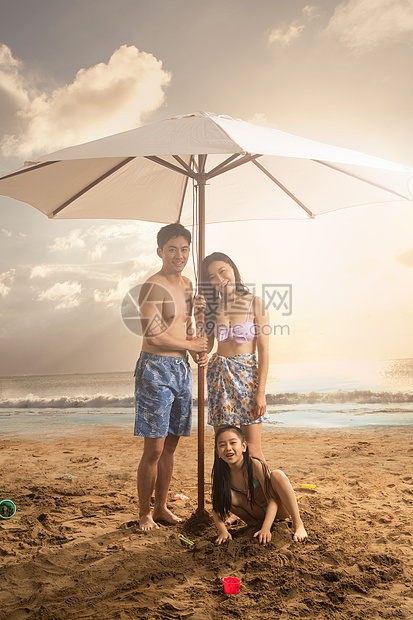 海滩上躲在遮阳伞下的三口之家图片