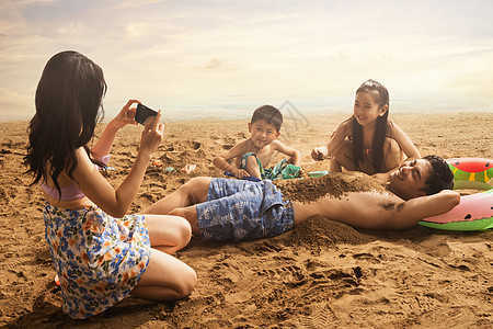 沙滩上青年女人为丈夫孩子拍照图片