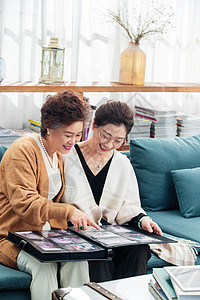 快乐的中老年姐妹坐在沙发上看相册图片