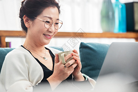 中老年女士拿着杯子看笔记本电脑图片