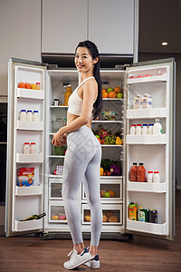 穿着运动装的青年女人站在冰箱前图片