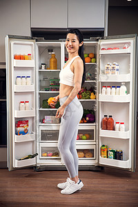 厨房家电穿着运动装的青年女人站在冰箱前背景