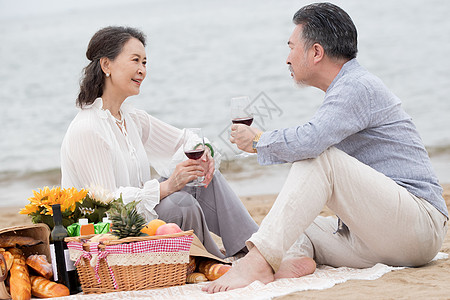 幸福的老年夫妇坐在海滩上野餐饮酒高清图片