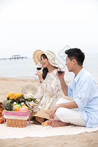 浪漫的青年夫妇坐在沙滩上喝红酒图片