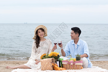 情侣野餐浪漫的青年夫妇坐在沙滩上喝红酒背景