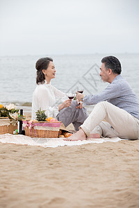 幸福的老年夫妇坐在海滩上野餐饮酒图片