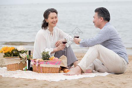 幸福的老年夫妇坐在海滩上野餐饮酒图片