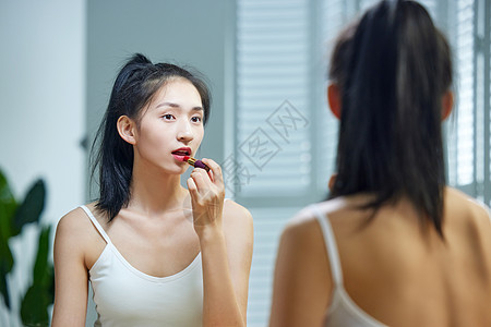 漂亮的年轻女人照着镜子涂口红图片