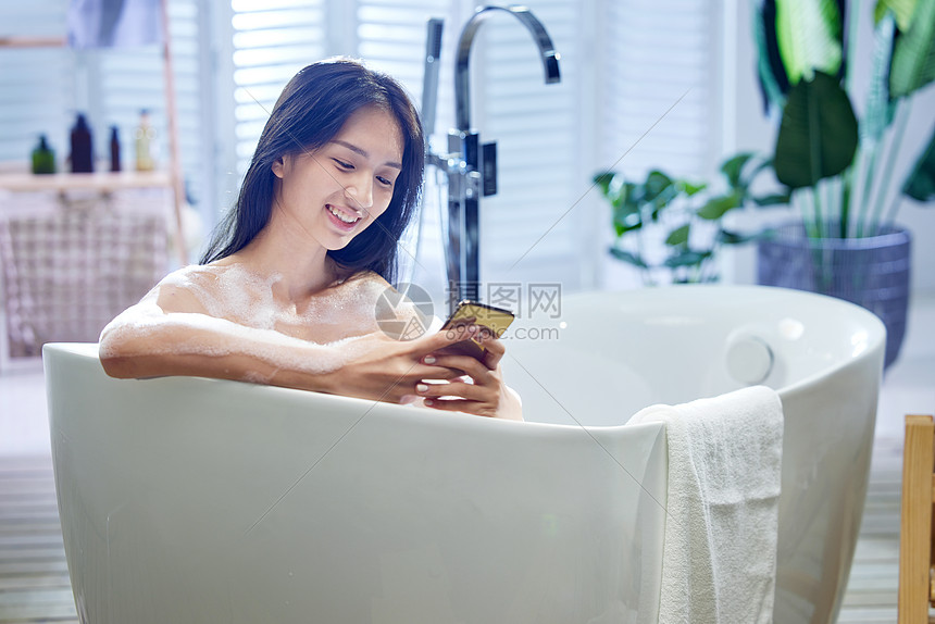 浴缸内使用手机的年轻女孩图片