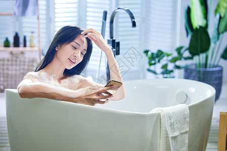 浴缸内使用手机的年轻女孩图片